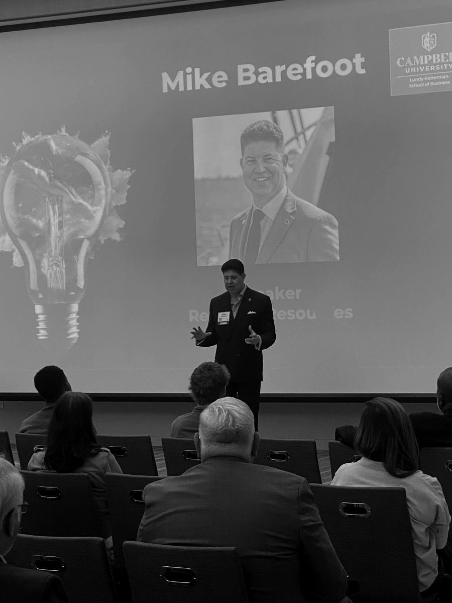 Mike Barefoot on stage at Campbell University, his name on the screen behind him